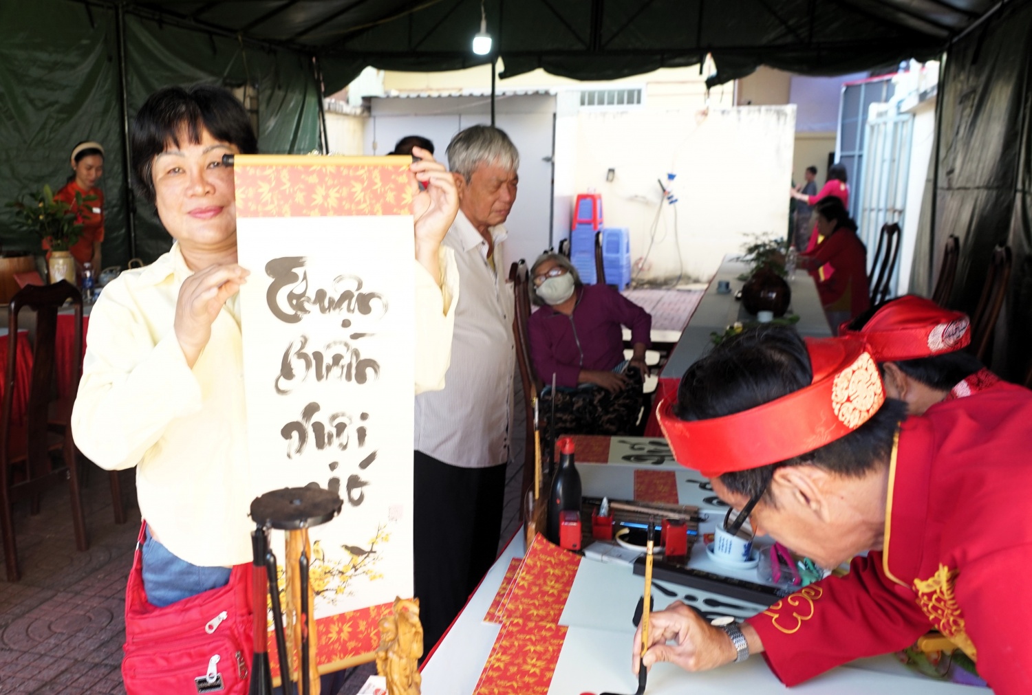 Cử tri Nguyễn Thị Chiêm phấn khởi nhận chữ thư pháp “Tâm - Đức - Nhẫn” sau khi hoàn thành bỏ phiếu tại điểm bỏ phiếu số 3. Hoạt động tặng chữ đầu xuân được tổ chức ngay tại khu vực bầu cử, tạo thêm không khí trang trọng và ý nghĩa trong ngày hội toàn dân.