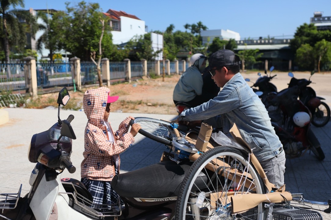 Em học sinh phụ ba cột chiếc xe đạp mới để chở về nhà.